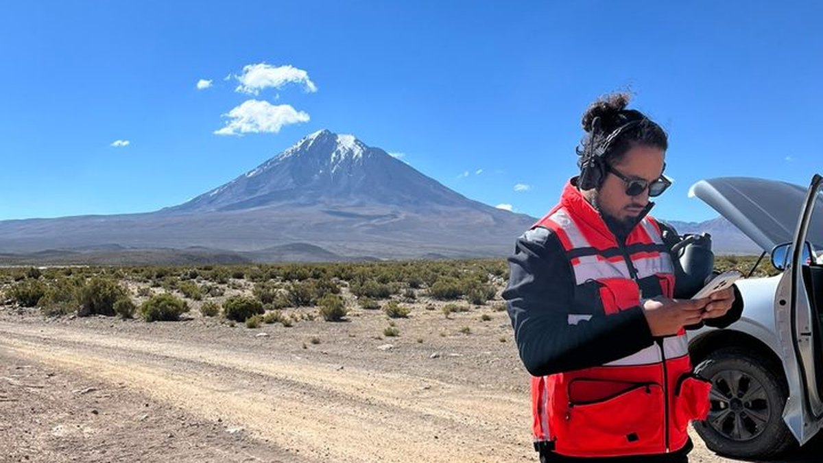 Piloto de AÉREO planificando un vuelo en terreno, con chaleco reflectante y el control en la mano, junto al vehículo de la operación