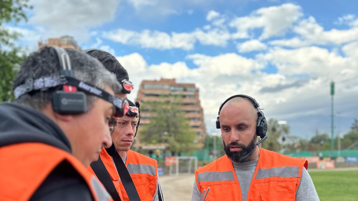 Instructor de AÉREO frente a un grupo de alumnos de los Niveles 2 y 3, todos con chaleco reflectante, linterna frontal e intercomunicador, bajo un cielo despejado