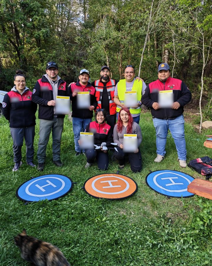 Voluntarios del Cuerpo de Bomberos de Curacautín con el diploma del curso de piloto de drones, frente a tres plataformas de aterrizaje