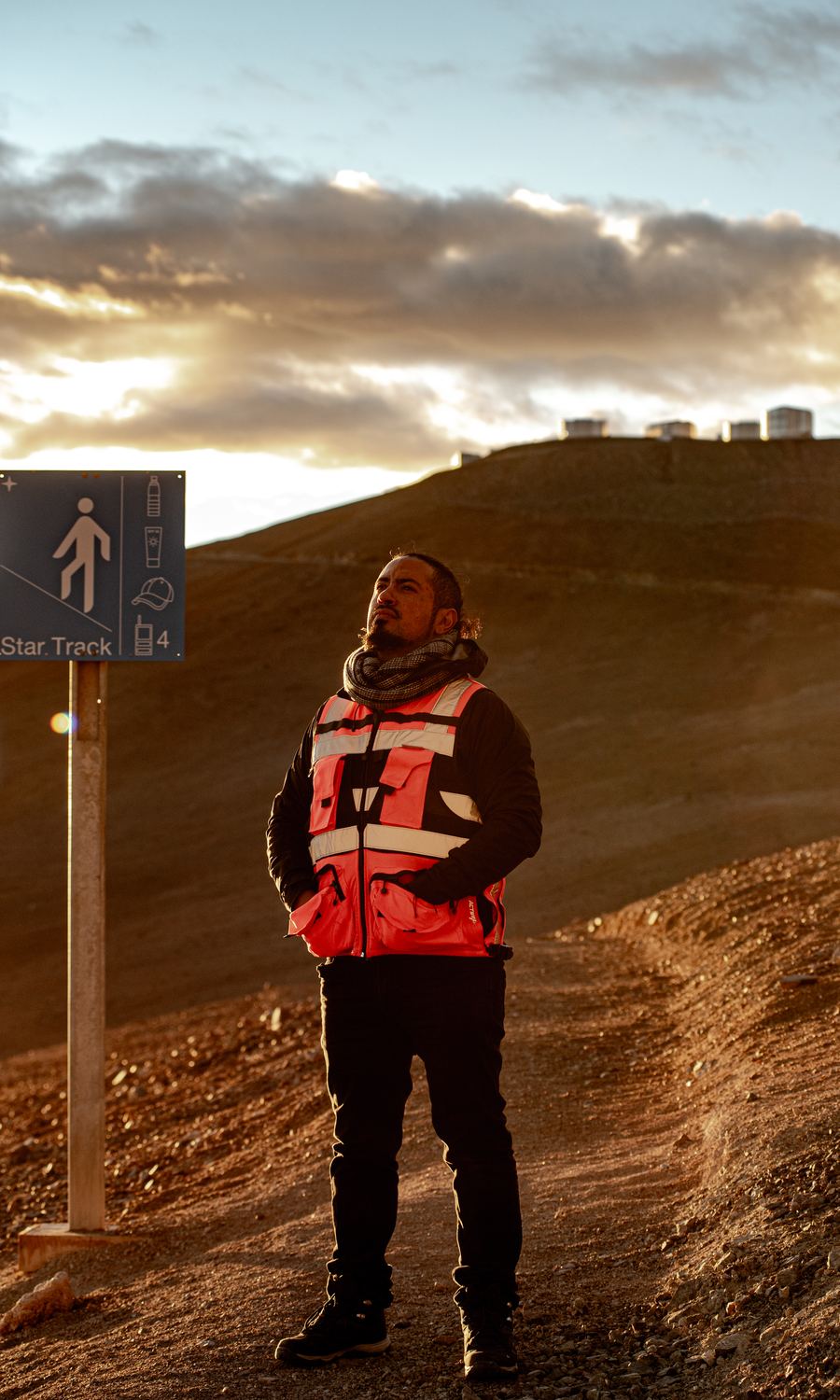 Piloto de AÉREO al atardecer junto a la señalética del observatorio, con el cerro Paranal detrás