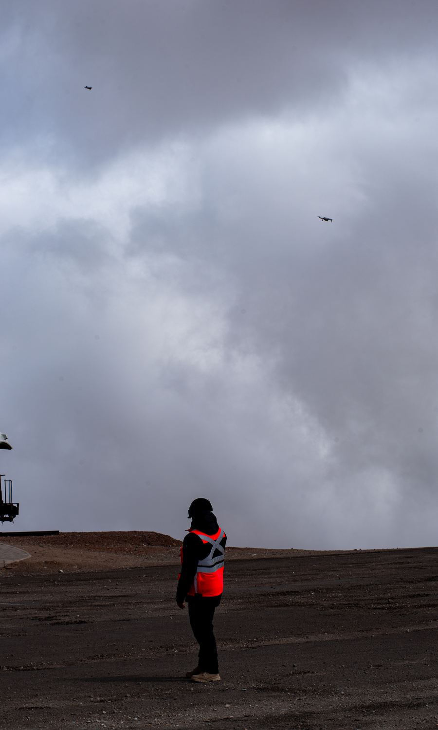 Piloto con chaleco reflectante manteniendo contacto visual con dos drones bajo un cielo completamente nublado en Paranal