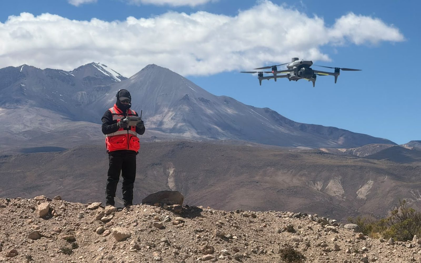 Piloto operando el dron desde un cerro del altiplano, con el dron en vuelo a su derecha