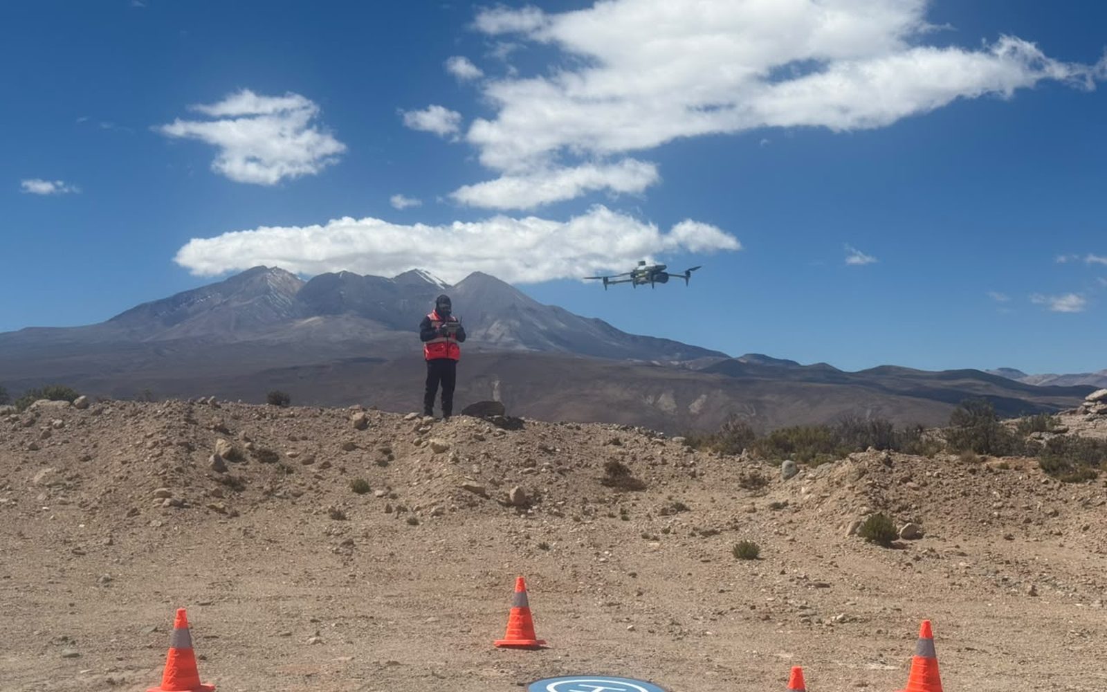 Zona de despegue señalizada con conos y plataforma en el altiplano, con el dron en el aire y los cerros al fondo