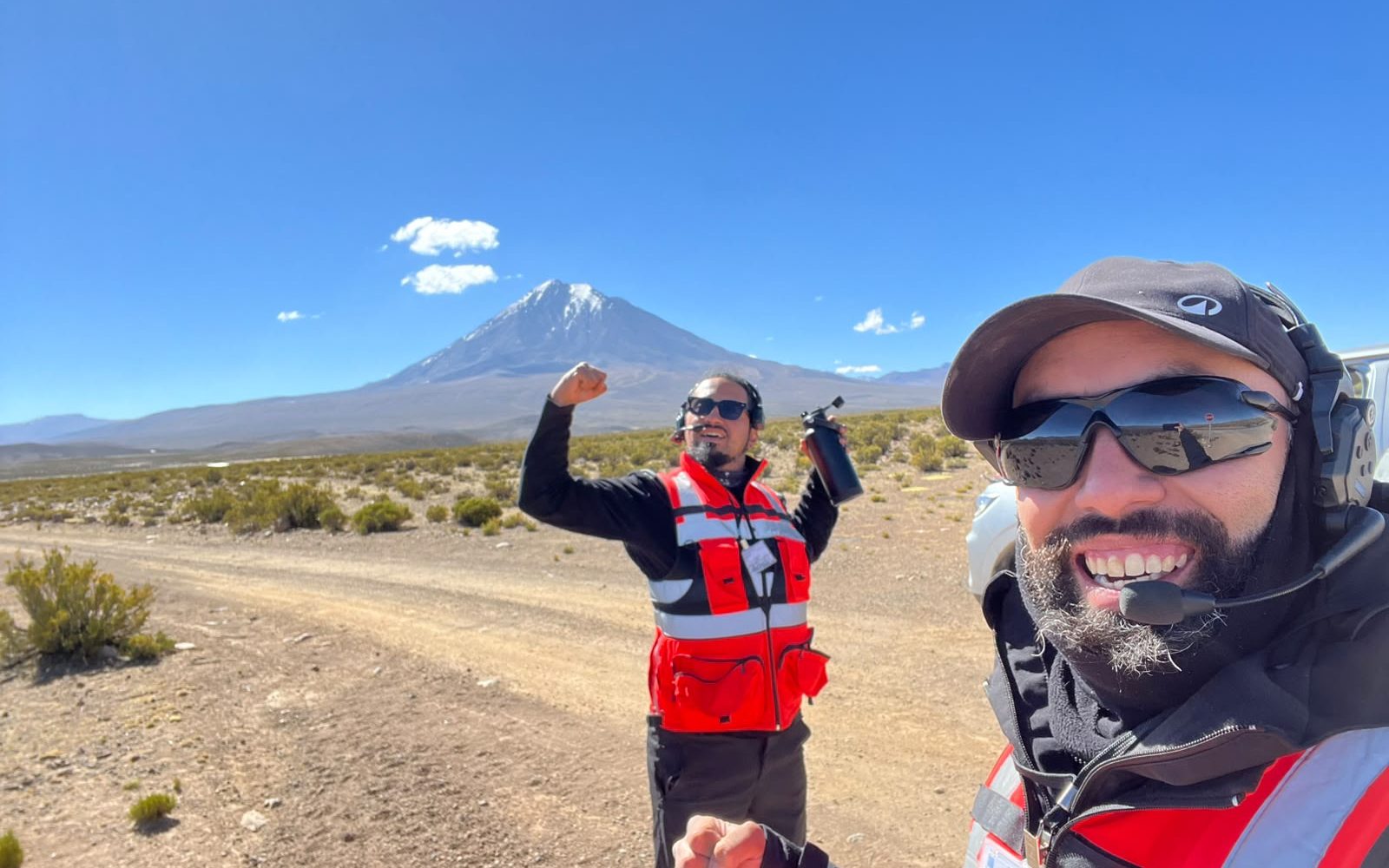 Los dos pilotos de AÉREO en terreno, con chaleco reflectante y el volcán nevado al fondo